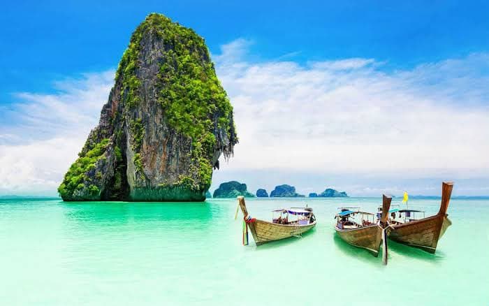 Two wooden longtail boats on turquoise water beside limestone karsts
